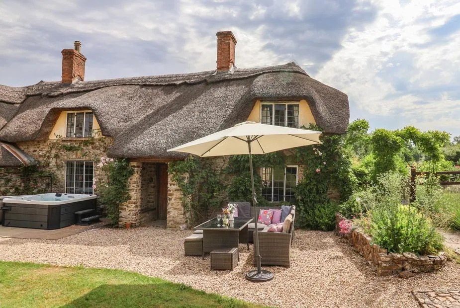 Traditional stone holiday cottage featuring a hot tub and patio with an umbrella