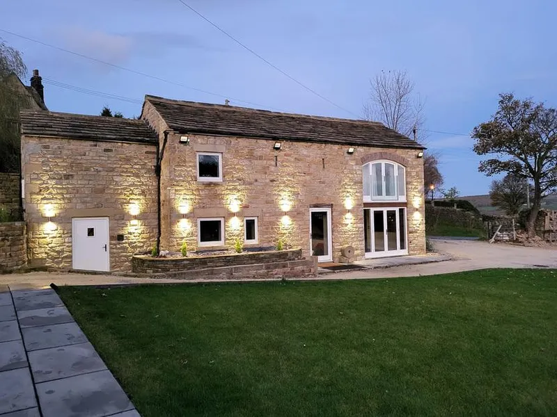 Green Barn stone barn conversion lit by wall lights at dusk with lawned garden and countryside beyond