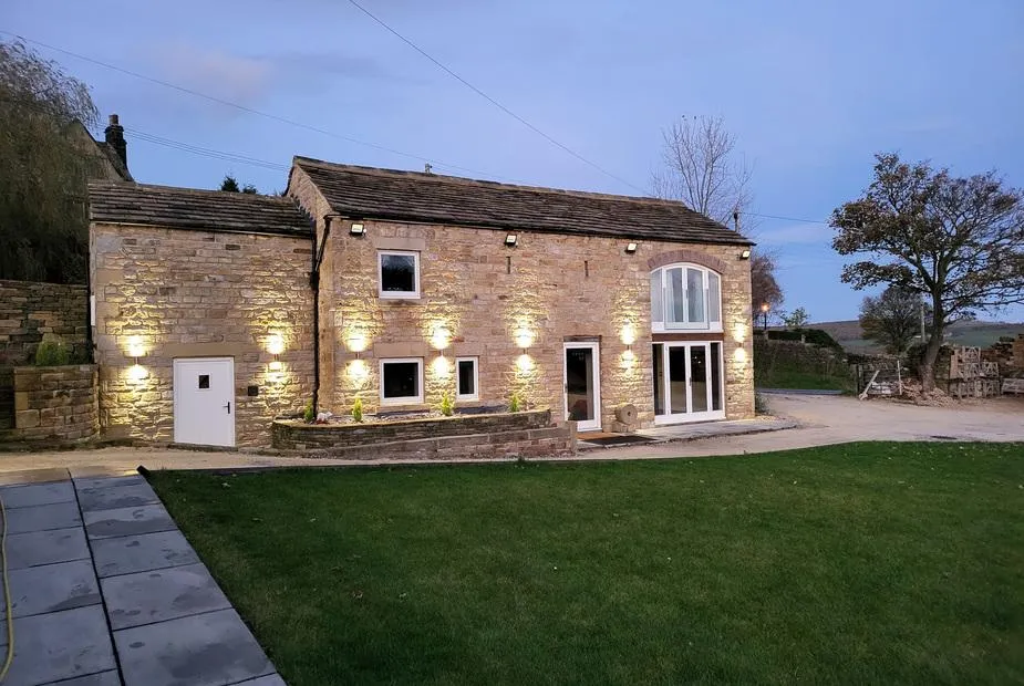 Green Barn stone barn conversion lit by wall lights at dusk with lawned garden and countryside beyond