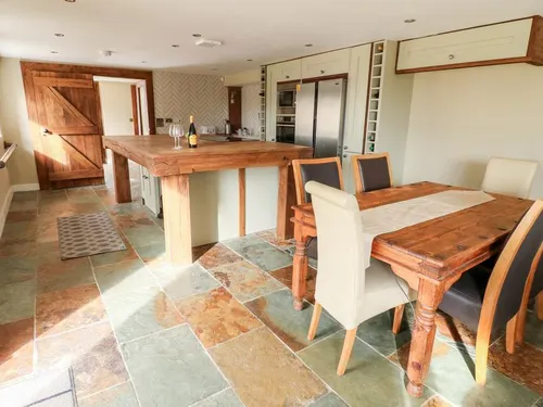 Open-plan kitchen and dining area with railway sleeper island, wooden dining table, and stone flag floors