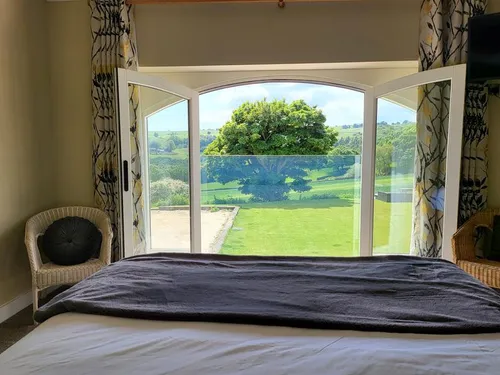 King-size bedroom with arched French doors opening to glass balustrade and valley views across green fields
