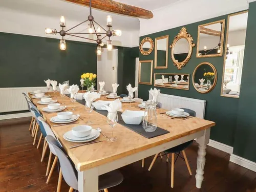 Cottage dining room with long table, set for twelve, and wall decorated with mirrors