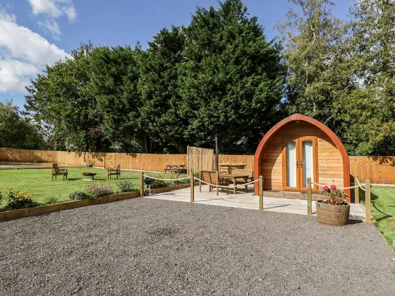 Halmore Pod with outdoor seating area and surrounding garden under large trees