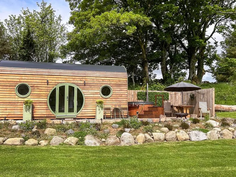 Heather lodge with round windows and outdoor hot tub in a garden setting
