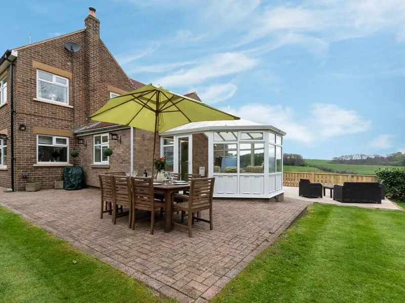 High Croft exterior with patio dining set, large parasol, and conservatory overlooking fields