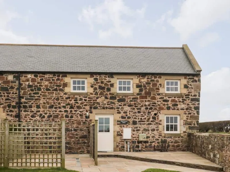 Stone exterior of High Hemmel House with fenced patio and hedgerow.
