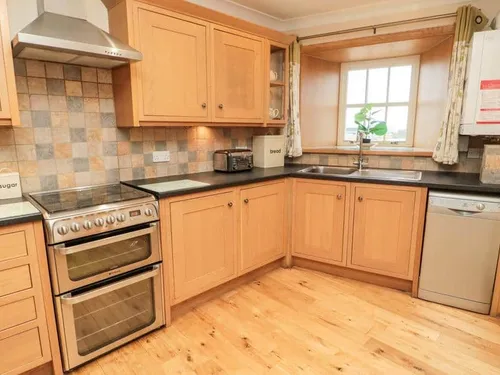 Cottage kitchen with wooden cabinets, range cooker and window above sink