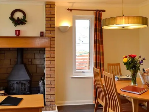Dining area with wooden table, chairs, and log burner in brick fireplace