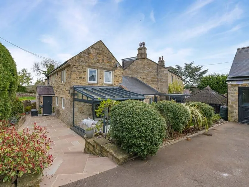 John's Cottage stone exterior with glass sunroom and landscaped garden shrubs