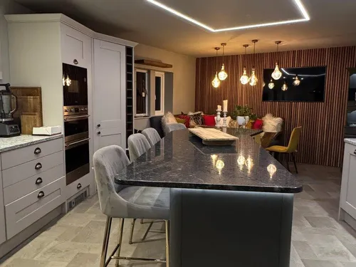 Kitchen diner with dark granite island, velvet bar stools, globe pendant lights, and wood-panelled dining wall
