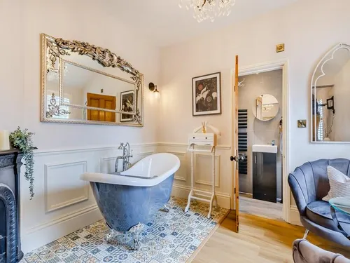 Master bedroom with blue slipper bath, ornate mirror, cast-iron fireplace, and en-suite shower room beyond