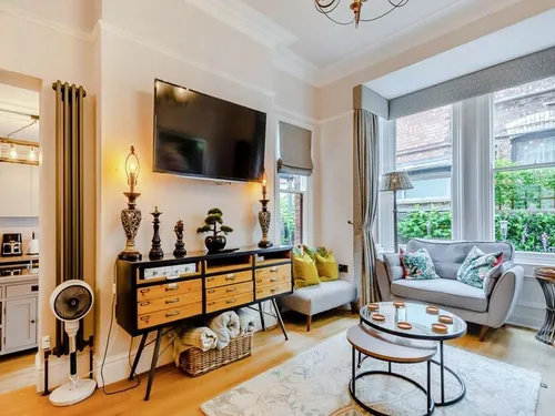 Living room with wall-mounted TV, vintage sideboard, grey sofa by a bay window, and kitchen beyond