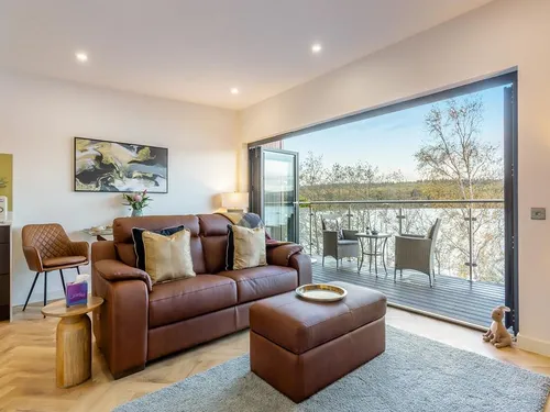 Contemporary open-plan living room with leather sofa and bi-fold doors opening onto a balcony overlooking Loch Ness