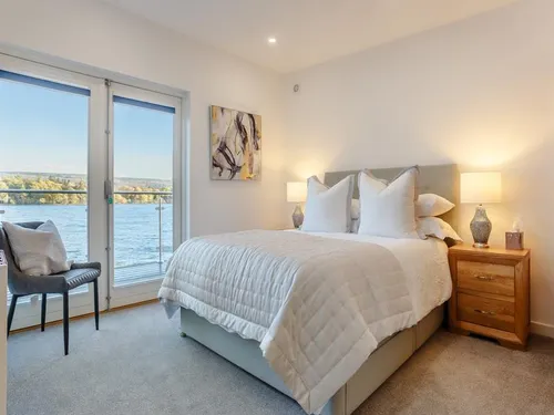 King-size bedroom with crisp white bedding and floor-to-ceiling loch views through glass doors