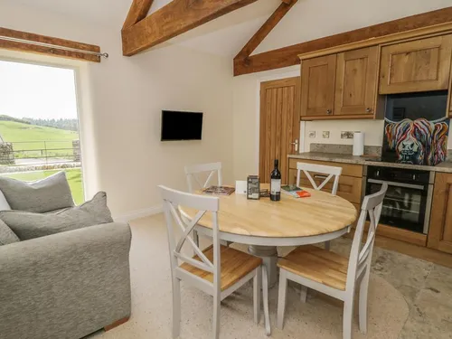 Open-plan living area with oak beams, grey sofa, dining table, and floor-to-ceiling countryside view