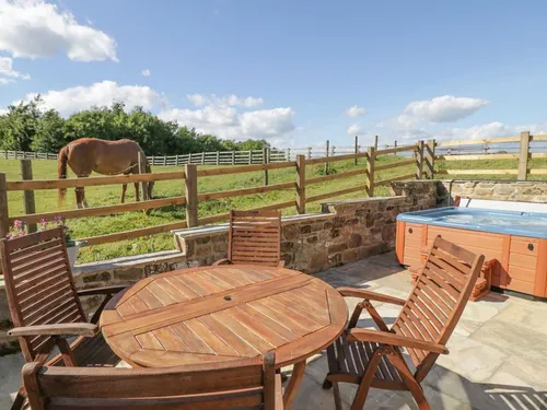Patio with wooden table, chairs, and hot tub overlooking fenced paddock with horse and countryside