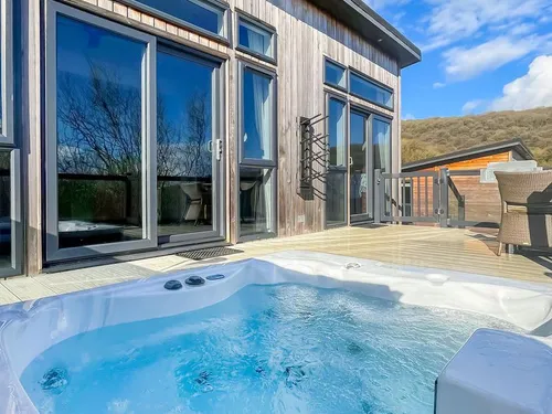 Hot tub on the timber deck with patio doors and Mendip Hills views behind the lodge