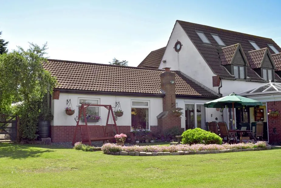 Leanda Lodge exterior with garden swing seat and patio dining area under a green umbrella