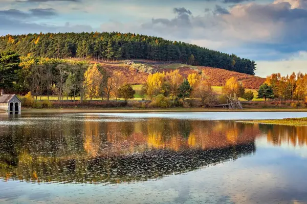 Autumn colours and a stone boathouse reflecting in the calm waters of Cropston Reservoir in Leicestershire.