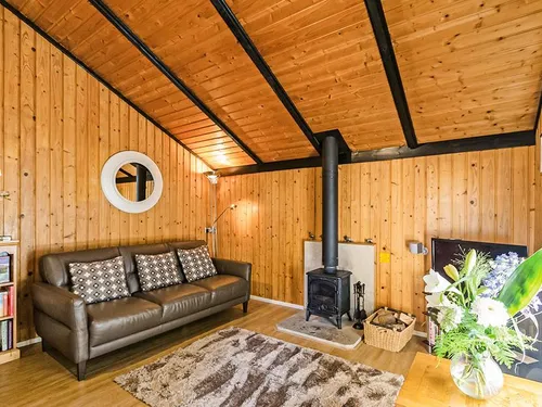 Pine-clad living room with leather sofa, log burner, and circular mirror at Lilleskov lodge