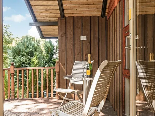 Covered decking with wooden chairs and a table overlooking treetops at Lilleskov lodge