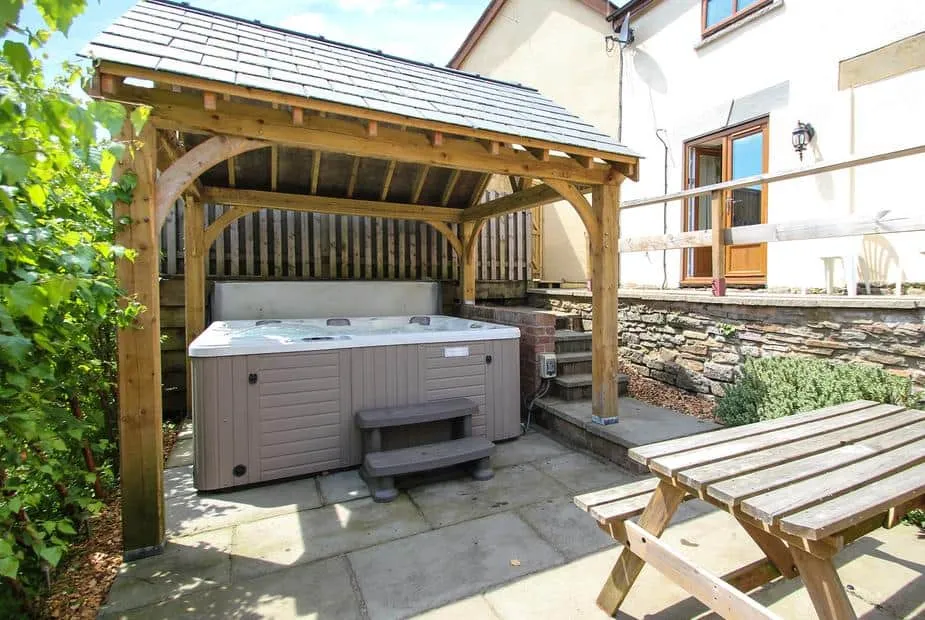 Lilly Cottage outdoor hot tub under wooden pergola with picnic bench nearby