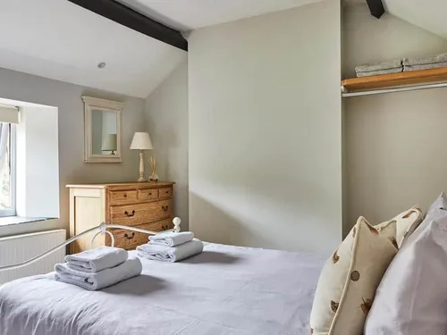 Cottage bedroom with double bed, wooden chest of drawers and open clothes shelf