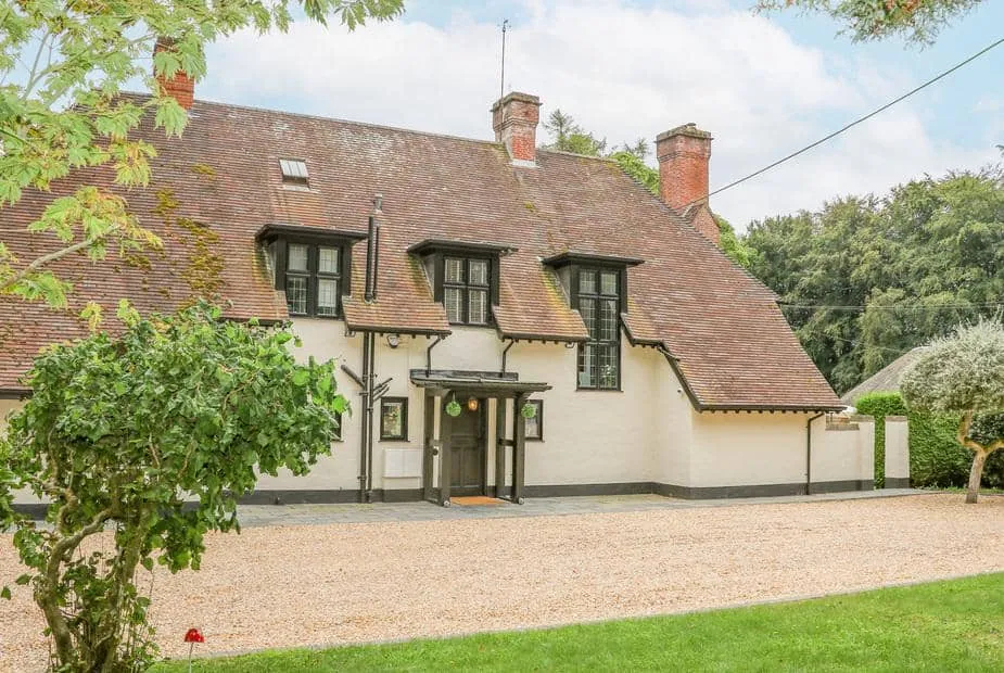 Little Picket cottage with steep tiled roof and gravel driveway in front garden.