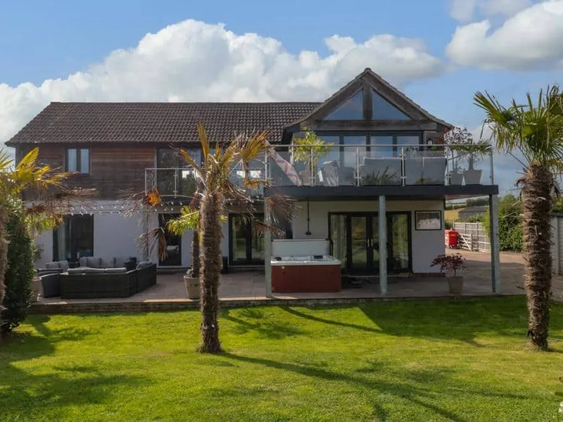 Longmynd cottage exterior with balcony, palm trees and outdoor hot tub on patio.