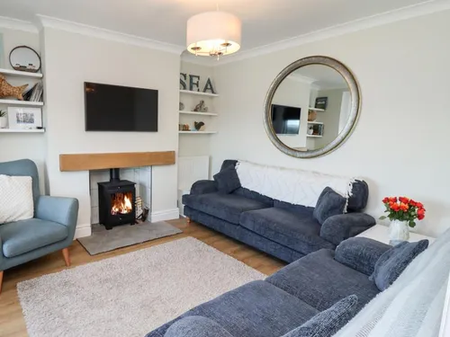 Sitting room with wood-burning stove, navy sofas, armchair, and wall-mounted TV