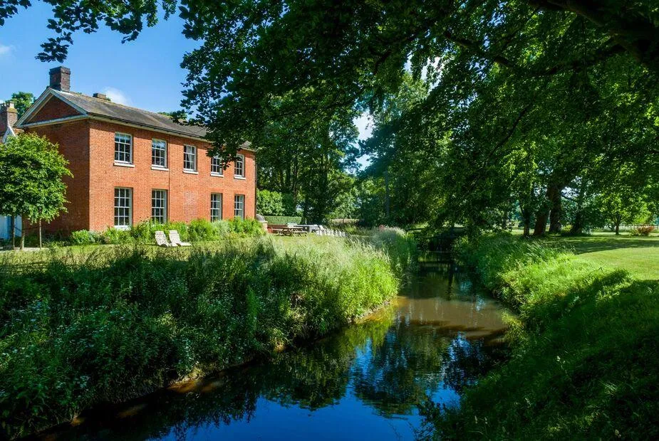 Meadowbrook Hall beside a stream with large trees and outdoor seating area