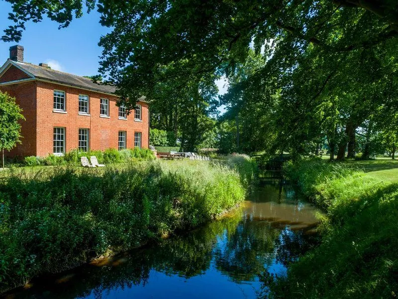 Meadowbrook Hall beside a stream with large trees and outdoor seating area