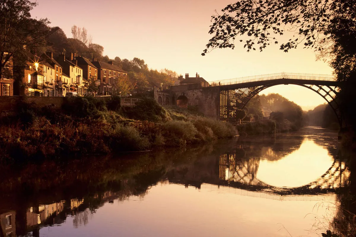 Golden sunset light illuminating the historic Iron Bridge crossing the River Severn in Shropshire, Midlands.