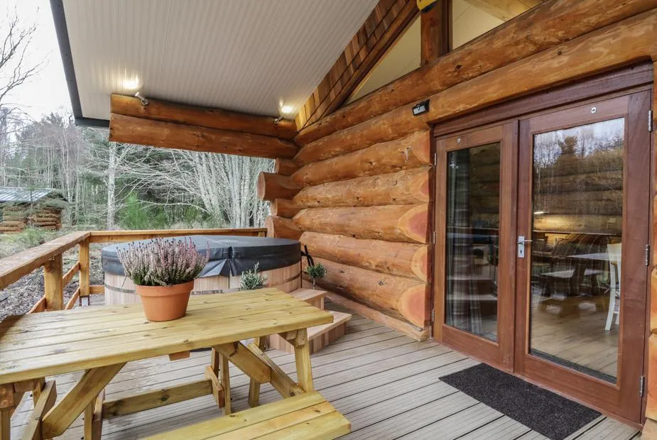 Log cabin deck with hot tub, picnic bench with heather, and woodland behind