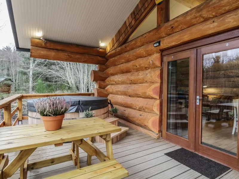 Log cabin deck with hot tub, picnic bench with heather, and woodland behind