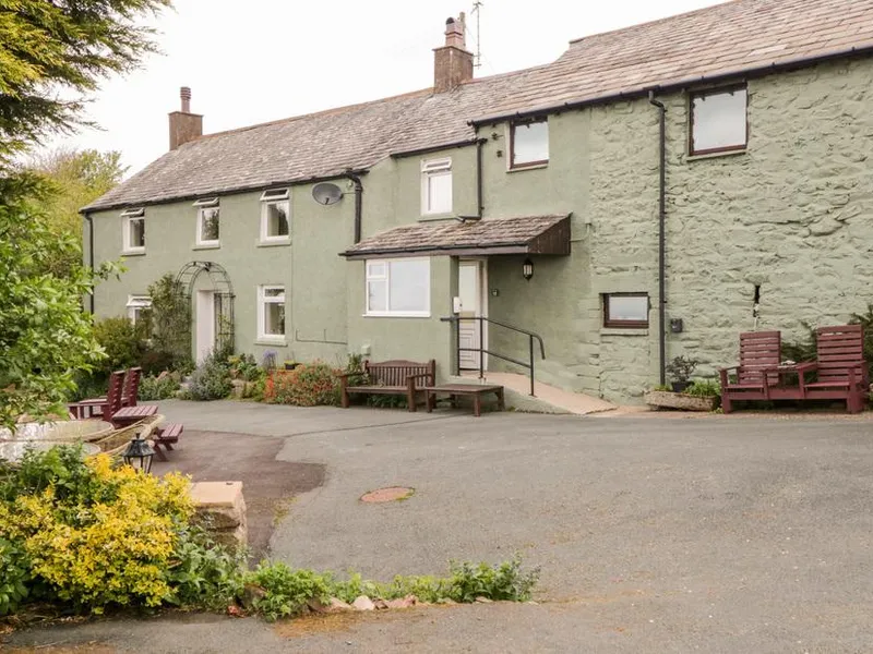 Near Bank Cottage exterior with stone walls and outdoor seating benches in front garden.