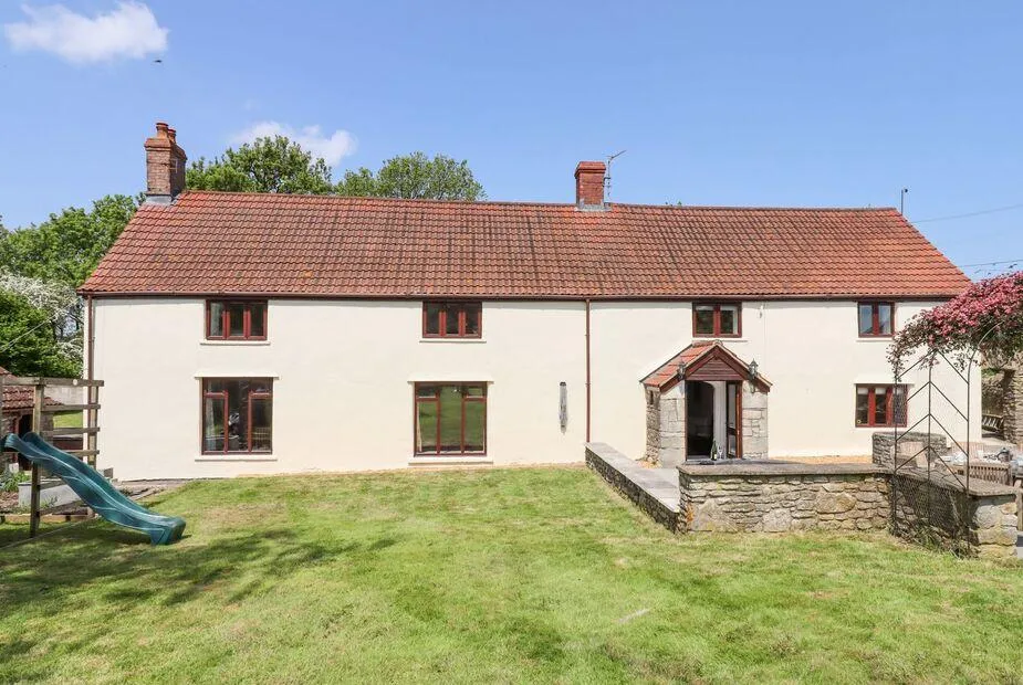 Nempnett Farmhouse rear exterior with cream rendered walls, stone porch, and children's slide on the lawn