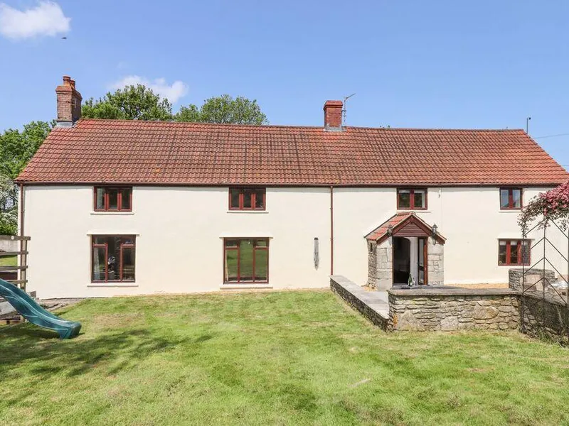 Nempnett Farmhouse rear exterior with cream rendered walls, stone porch, and children's slide on the lawn
