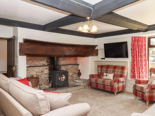 Sitting room with woodburning stove in a stone fireplace, tartan armchairs, and dark ceiling beams
