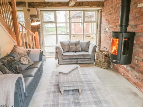 Cottage lounge with log burner, two sofas, footstool and exposed brick wall