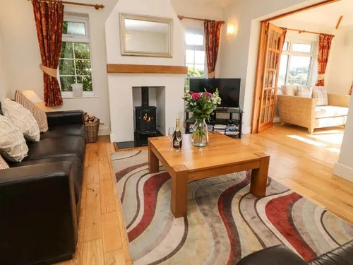 Cottage lounge with wood burner, leather sofa, and coffee table on patterned rug