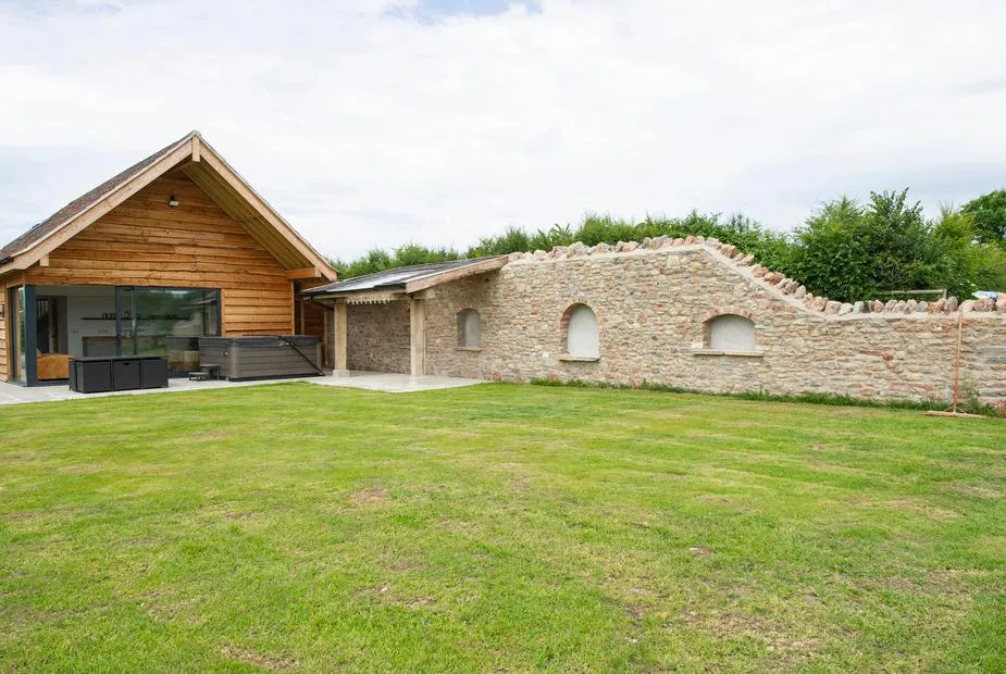 Owl Lodge timber-clad exterior with hot tub on the patio, lawn garden, and stone boundary wall