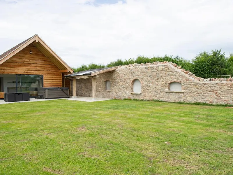 Owl Lodge timber-clad exterior with hot tub on the patio, lawn garden, and stone boundary wall