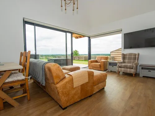 Open-plan living area with tan leather sofa, check wingback armchair, and bi-fold doors onto Somerset Levels views