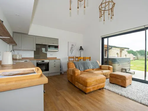 Open-plan kitchen with grey shaker cabinets, oak worktops, and tan leather seating facing bi-fold doors to the garden