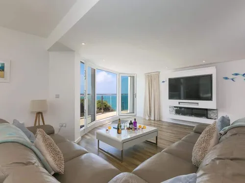 Cottage living room with corner sofas, large TV and sea view through open doors