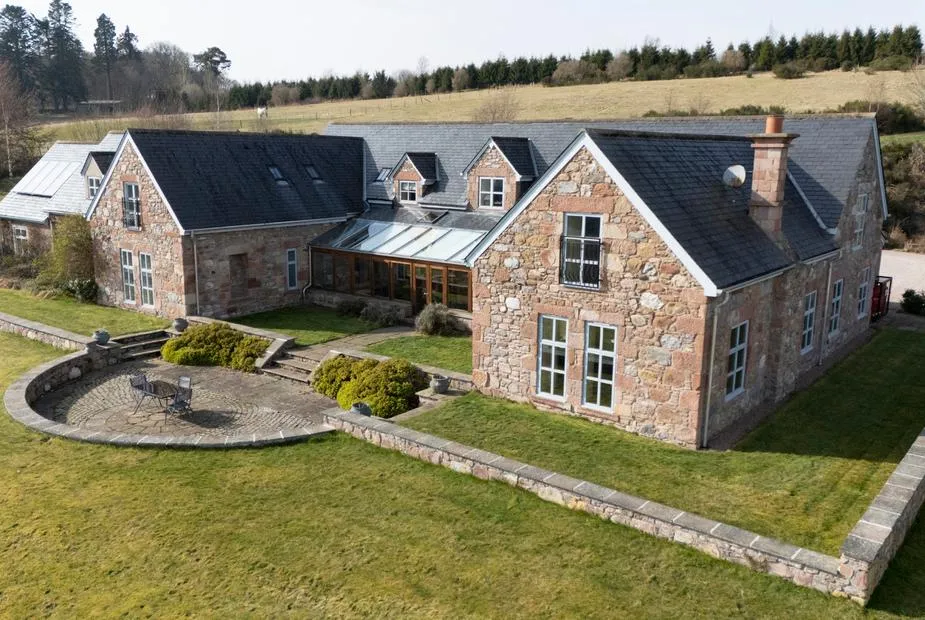 Aerial view of Quarryfield stone farmhouse with slate roof, glass atrium, and rolling Highland countryside