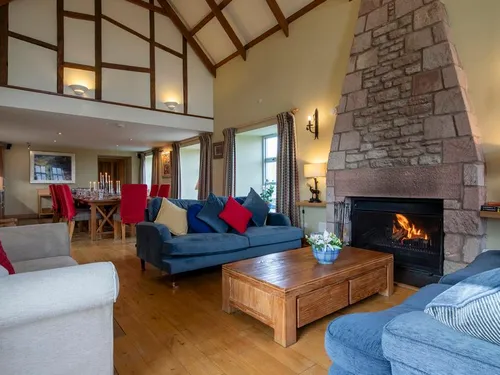 Open-plan living room with vaulted ceiling, stone fireplace, blue sofas, and dining area beyond