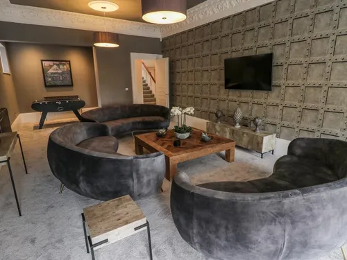 Gentleman's Lounge with dark velvet sofas, table football, wall-mounted TV, and textured feature wall