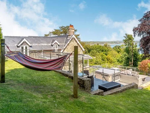 Hammock on lawn beside stone lodge with patio seating and hot tub